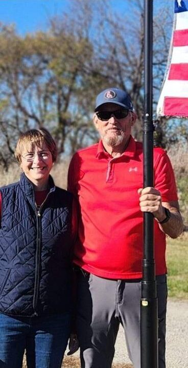 Steve and Sandy Lewis holding a flag pole flying the American Flag.